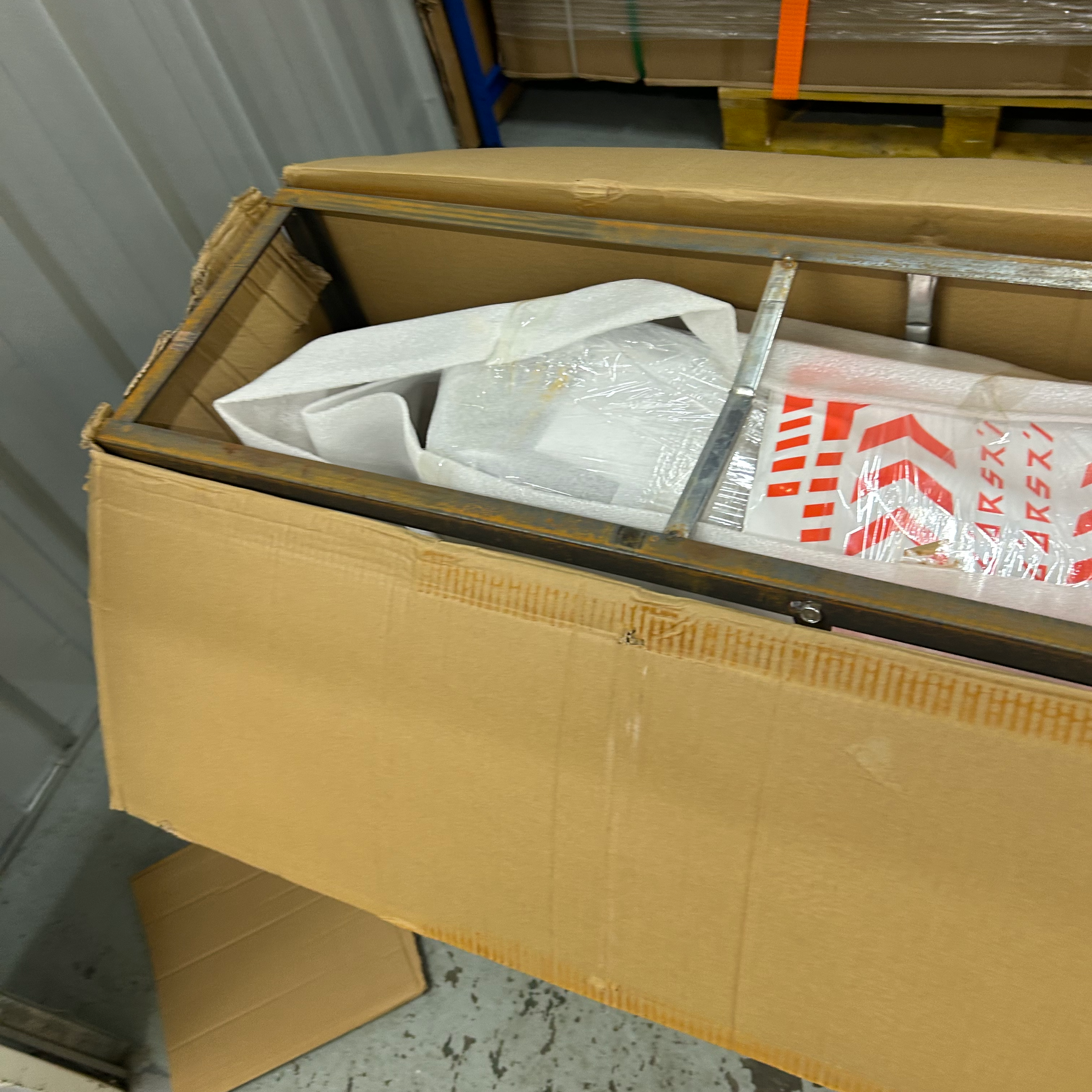 Open cardboard box with scooter contents on a concrete floor, possibly in a warehouse.