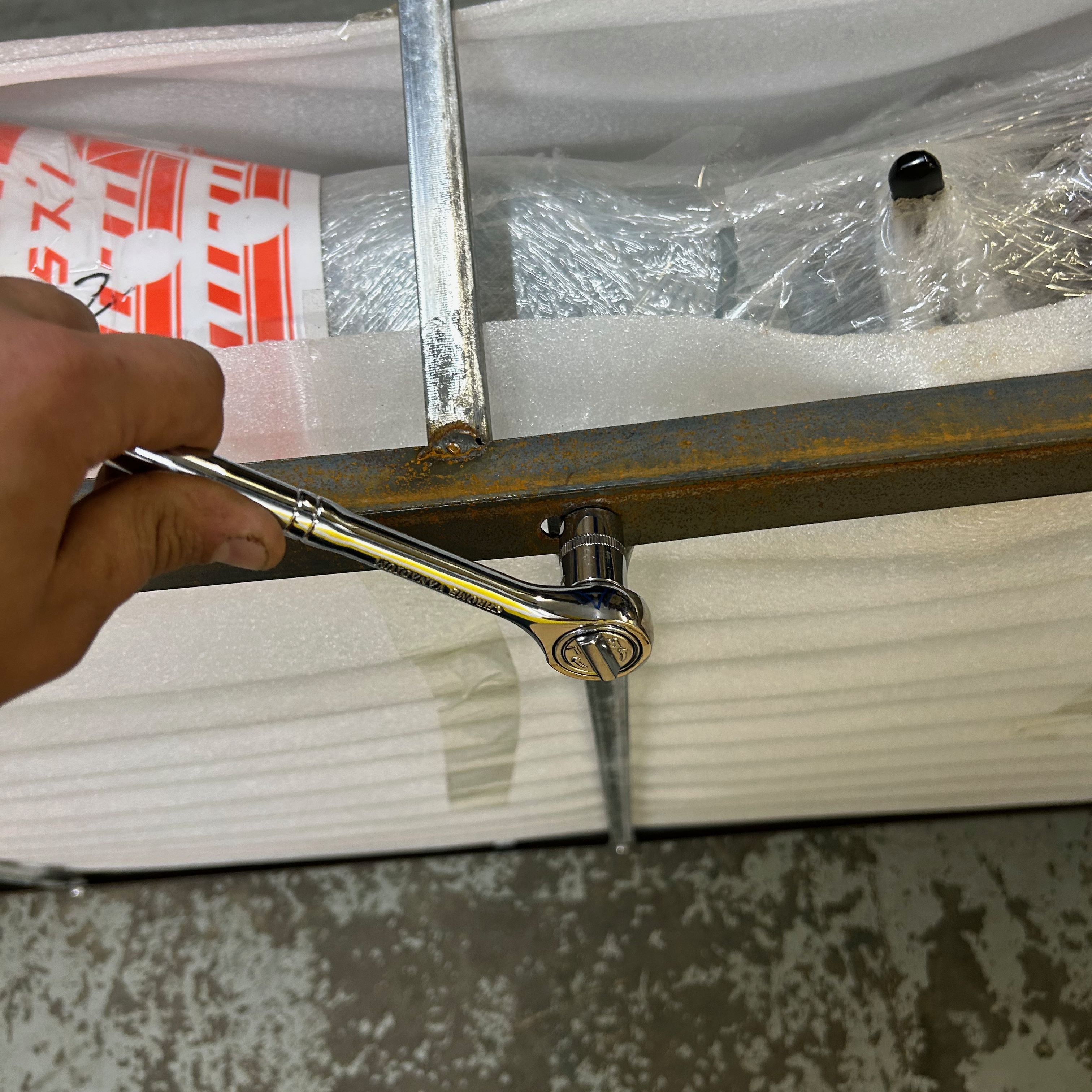 Person using a wrench to loosen a metal bracket on a piece of the metal frame