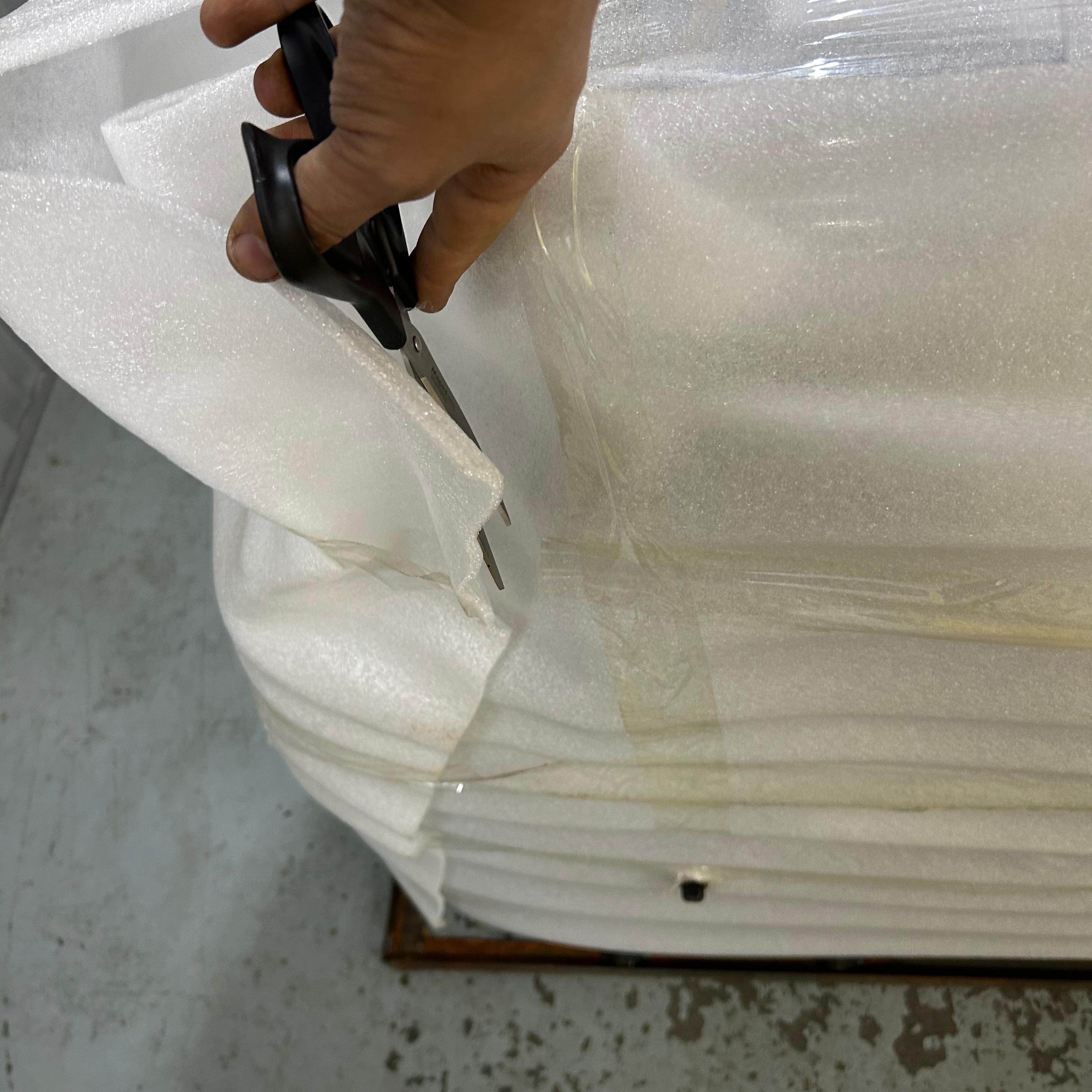 Hand cutting a stack of white foam wrapping with scissors on a concrete floor.