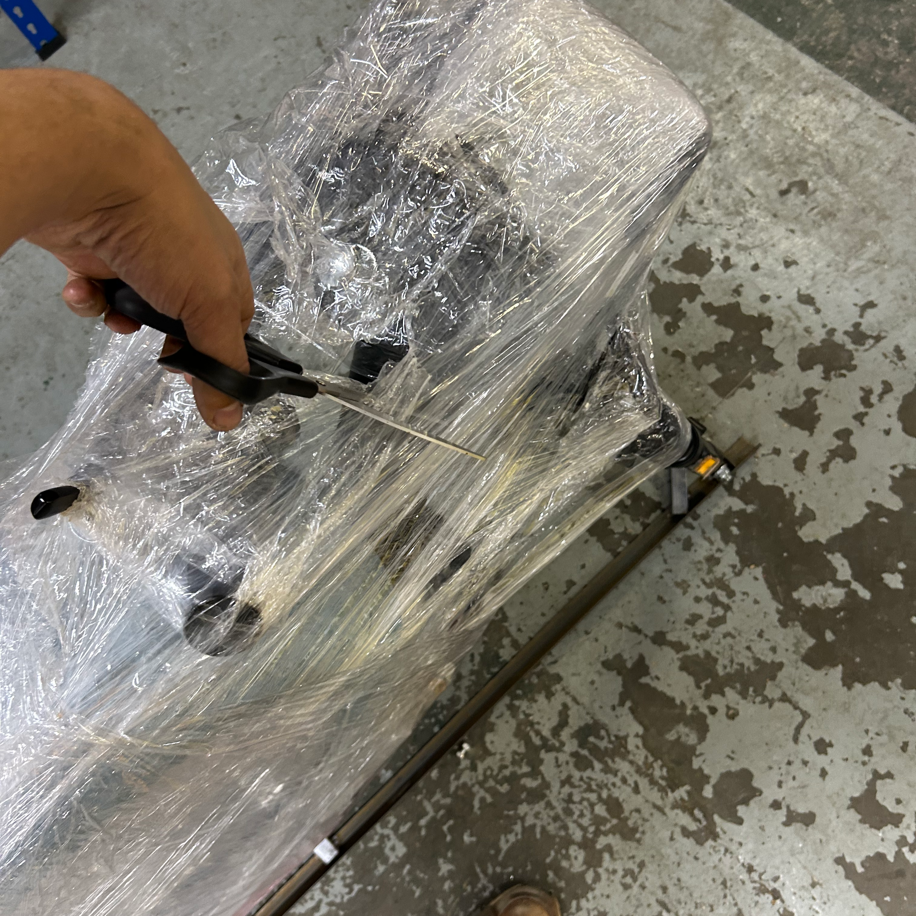 Person using a scissor on a wrapped scooter on a concrete floor