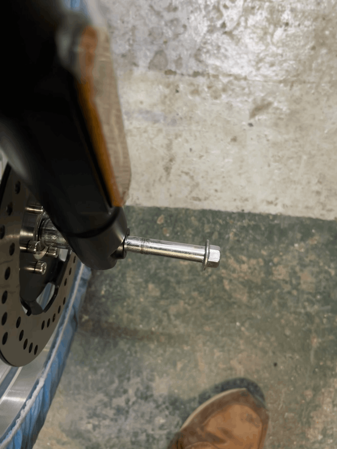 Close-up of a motorcycle wheel with a metal bolt on a concrete floor.