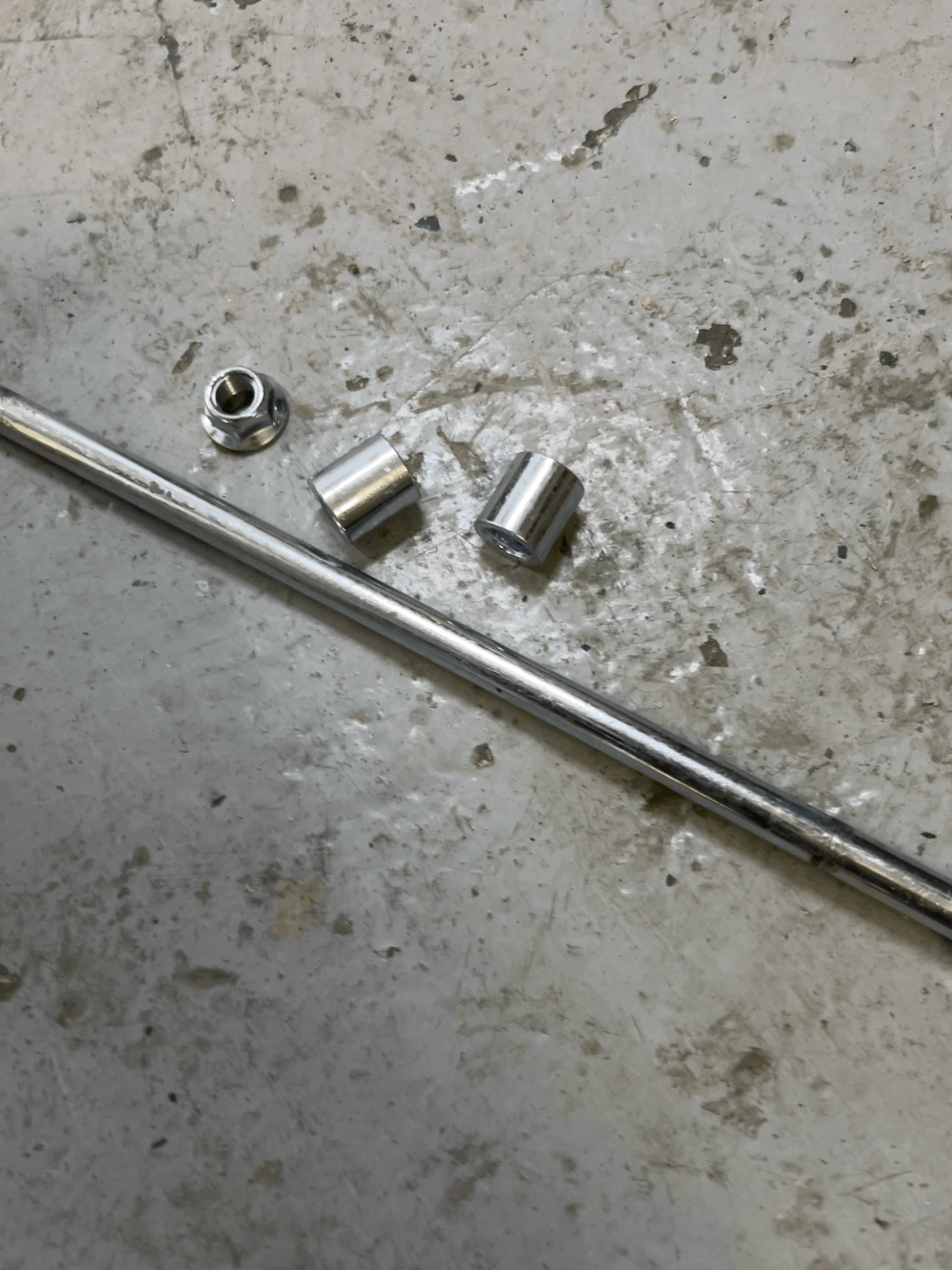 Metal rod with three cylindrical metal parts on a concrete surface