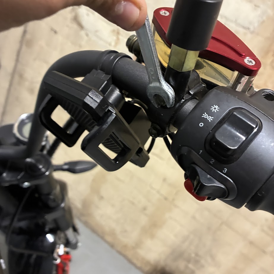 Close-up of a motorcycle handlebar with control levers and a wrench.