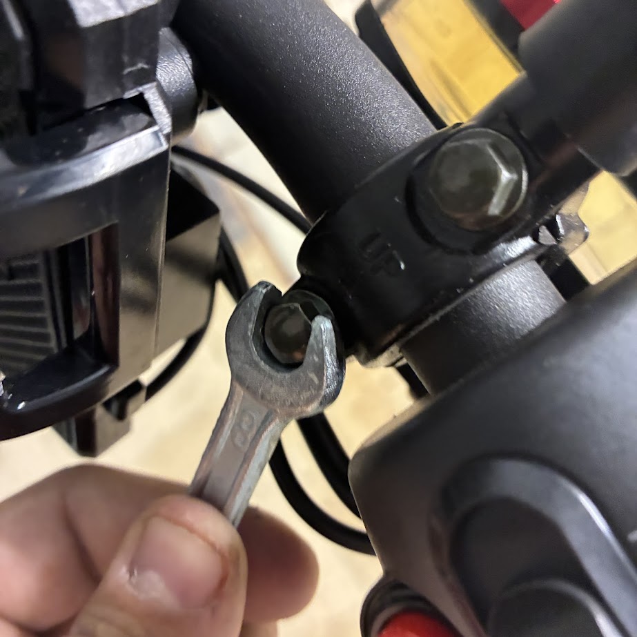 Person using a wrench on a motorcycle handlebar