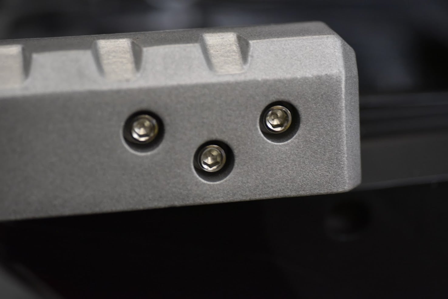 Close-up of a metallic object with three screws on a dark background