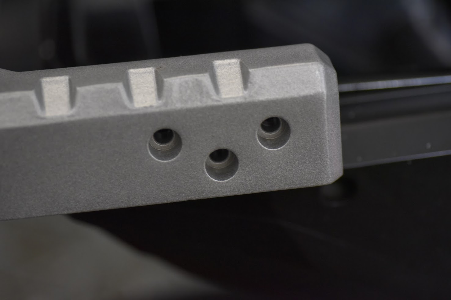 Close-up of a metallic bracket with threaded holes on a dark background
